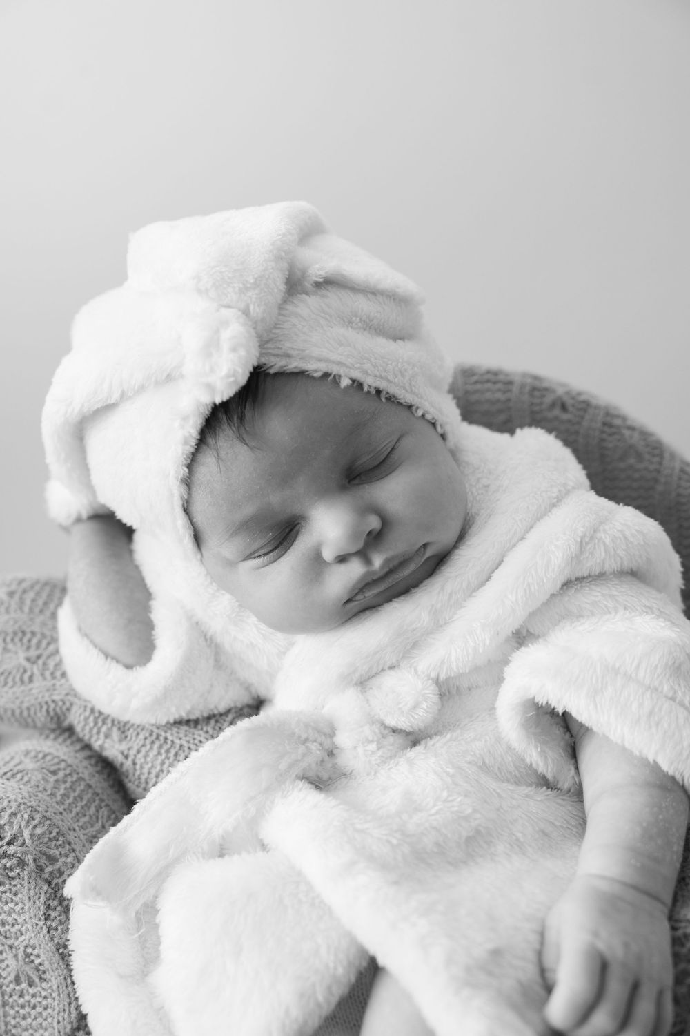 newborn photography session with baby posed on a couch and wearing a bath robe and headscarf.