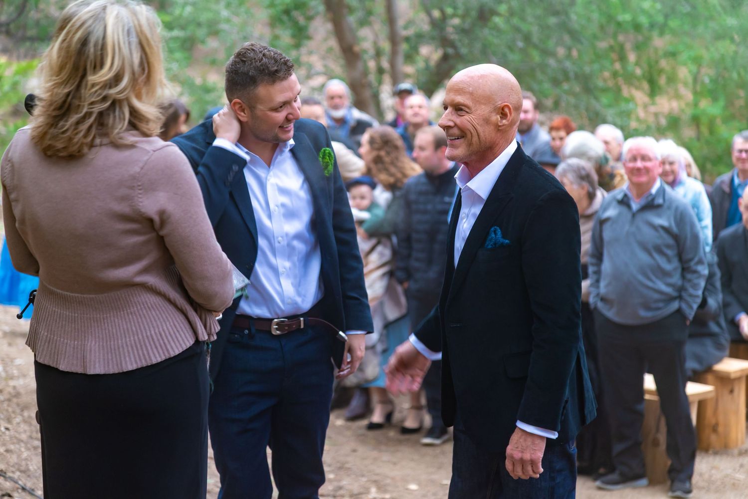 Outdoor wedding ceremony in a forest setting with guests seated, officiant and couple standing at the altar.