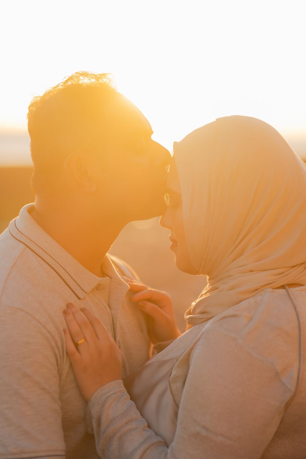 A couple sharing a tender moment at golden hour, woman wearing a hijab, bathed in warm sunset light.