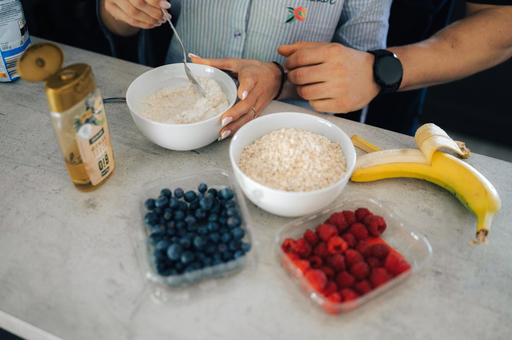 Hands preparing oatmeal with fresh blueberries, raspberries, and banana on a marble countertop.