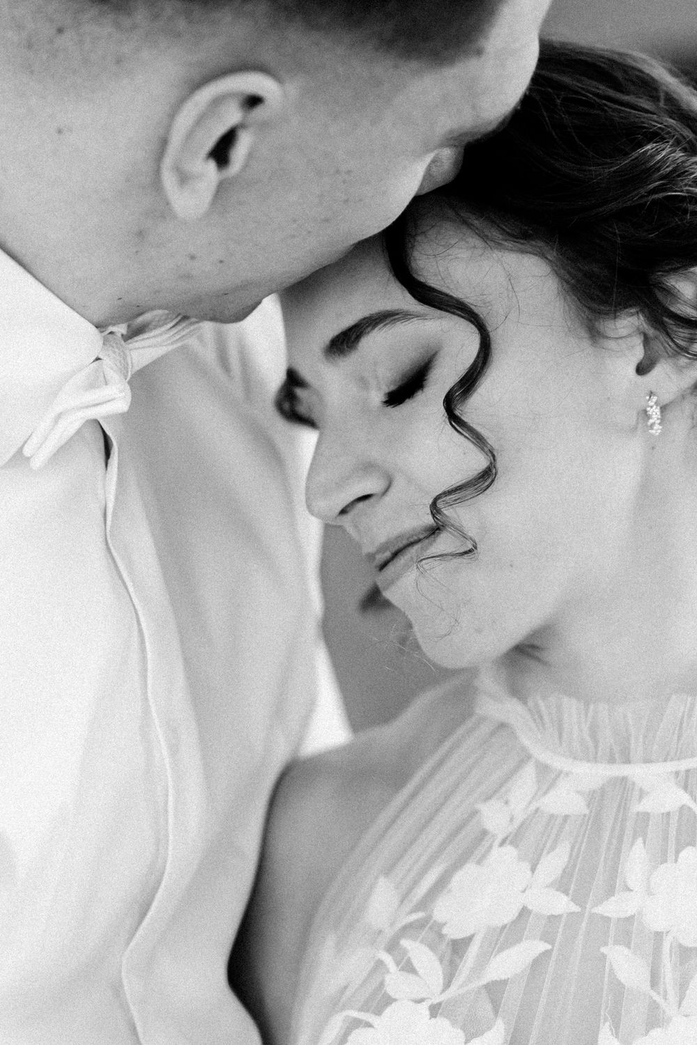 Black and white close-up of a romantic couple sharing an intimate moment in wedding attire.