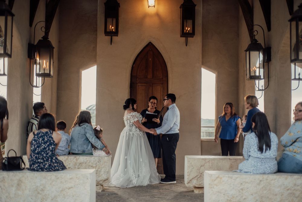 A small wedding ceremony takes place in a gothic-style chapel with lanterns and arched windows.