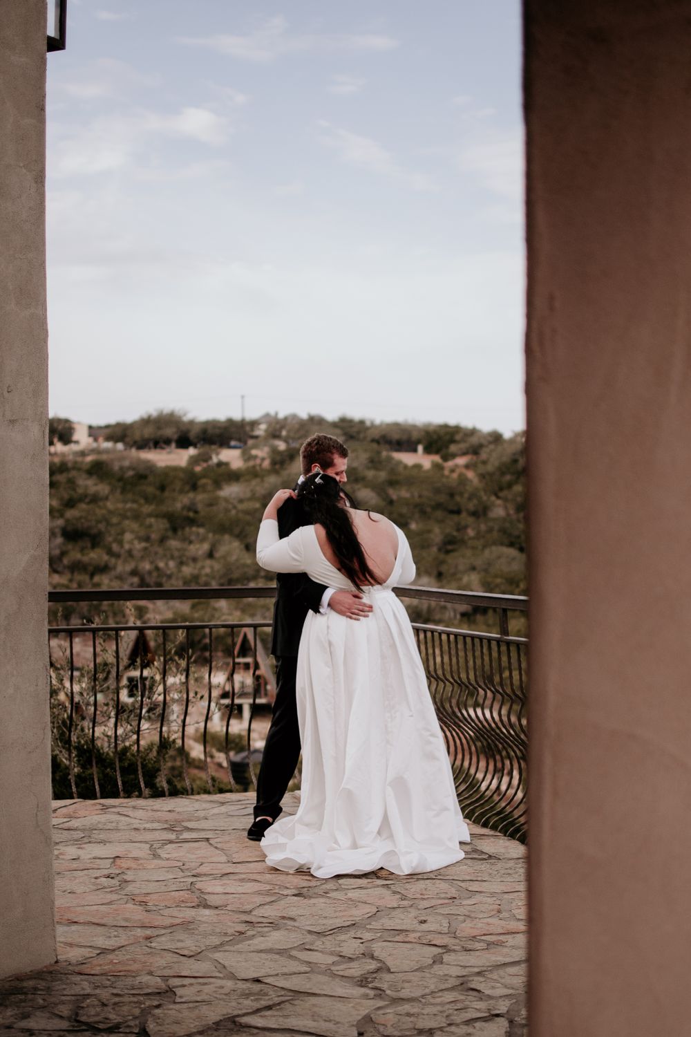 A romantic couple embraces on a stone patio overlooking a scenic vista during their wedding.