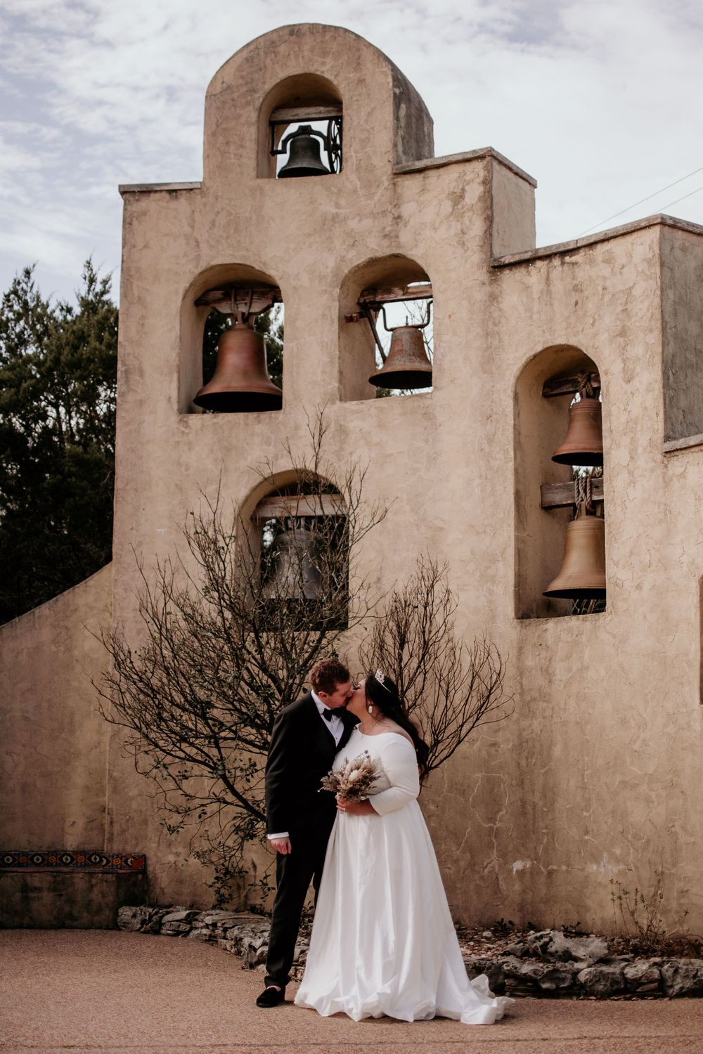 A romantic scene outside a Spanish Mission-style church with bell tower arches and desert landscaping.