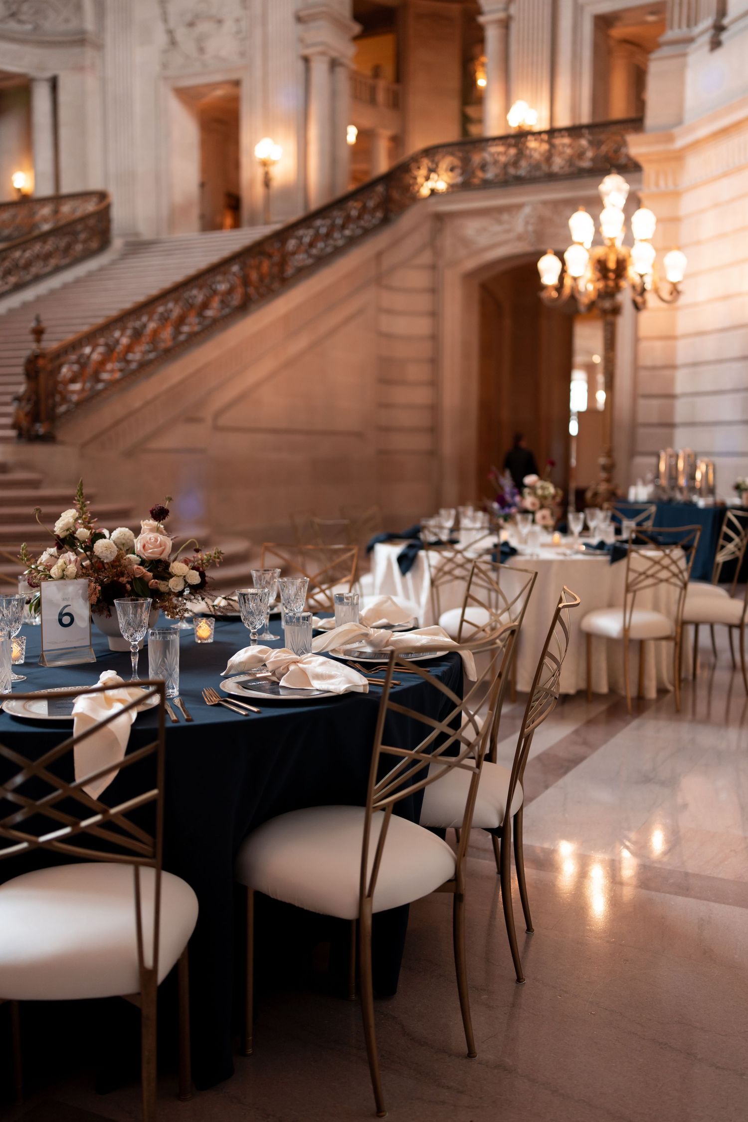 Two brides in elegant white gowns share a joyful moment on grand staircase in black and white wedding photo.