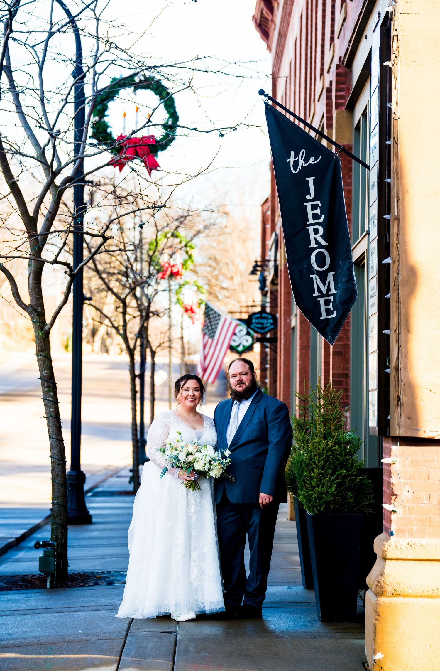Bride and groom posing outside The Jerome hotel with Christmas wreath decor on a sunny winter wedding day.