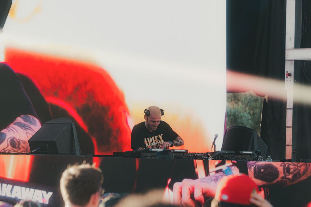 DJ performing on stage at an outdoor music festival with vibrant red and black backdrop lighting.