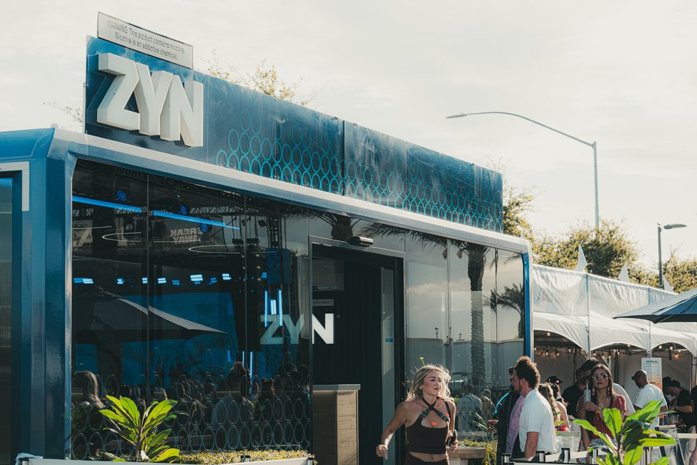 ZYN branded blue building exterior with people gathered outside at a sunny outdoor event or festival.