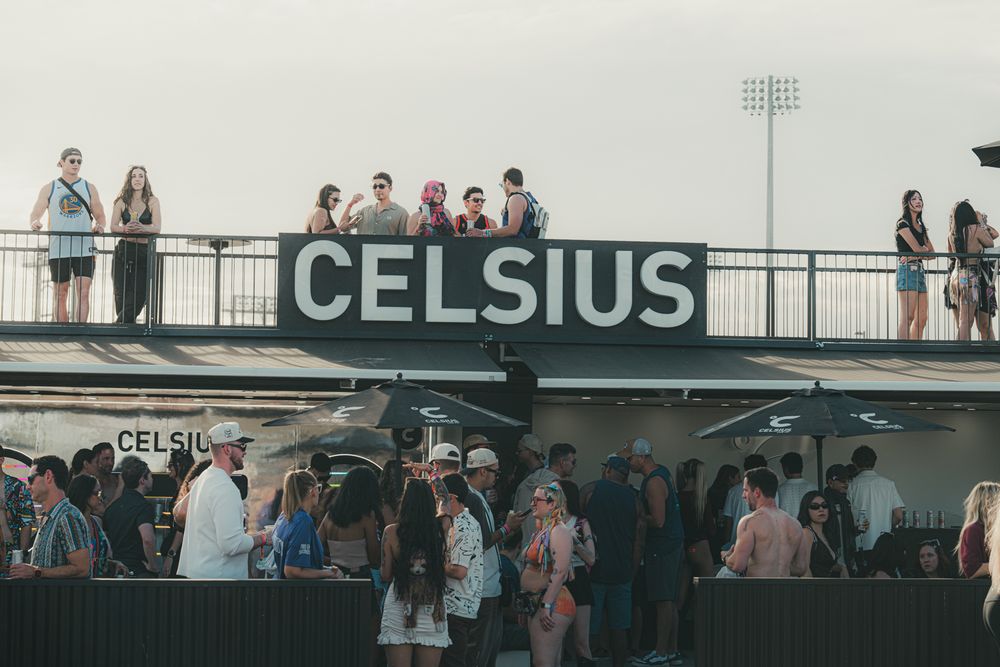 Crowd of festival-goers gathered beneath a large Celsius sign at an outdoor music festival event.