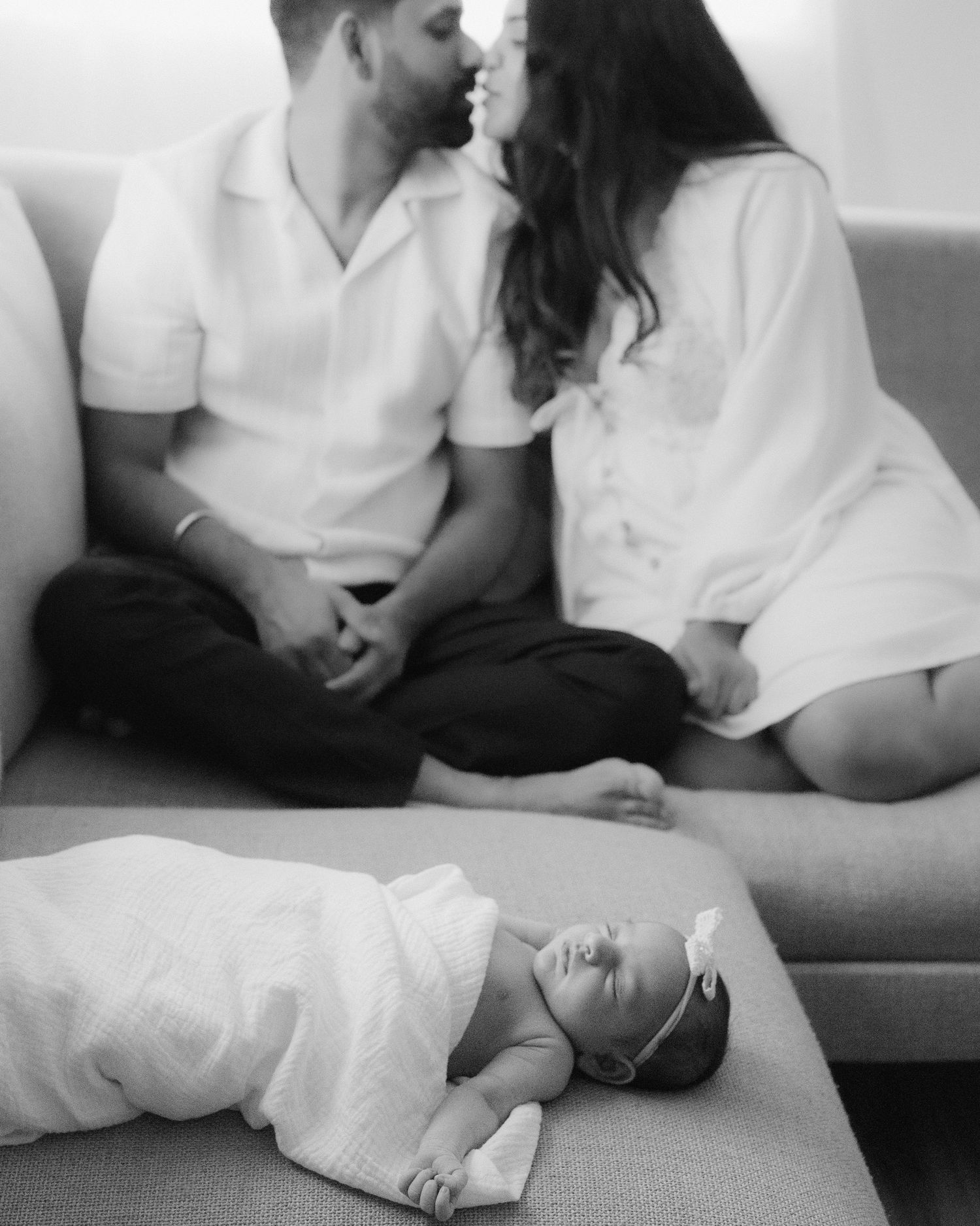 Parents kissing in background with focus on their newborn baby in the foreground