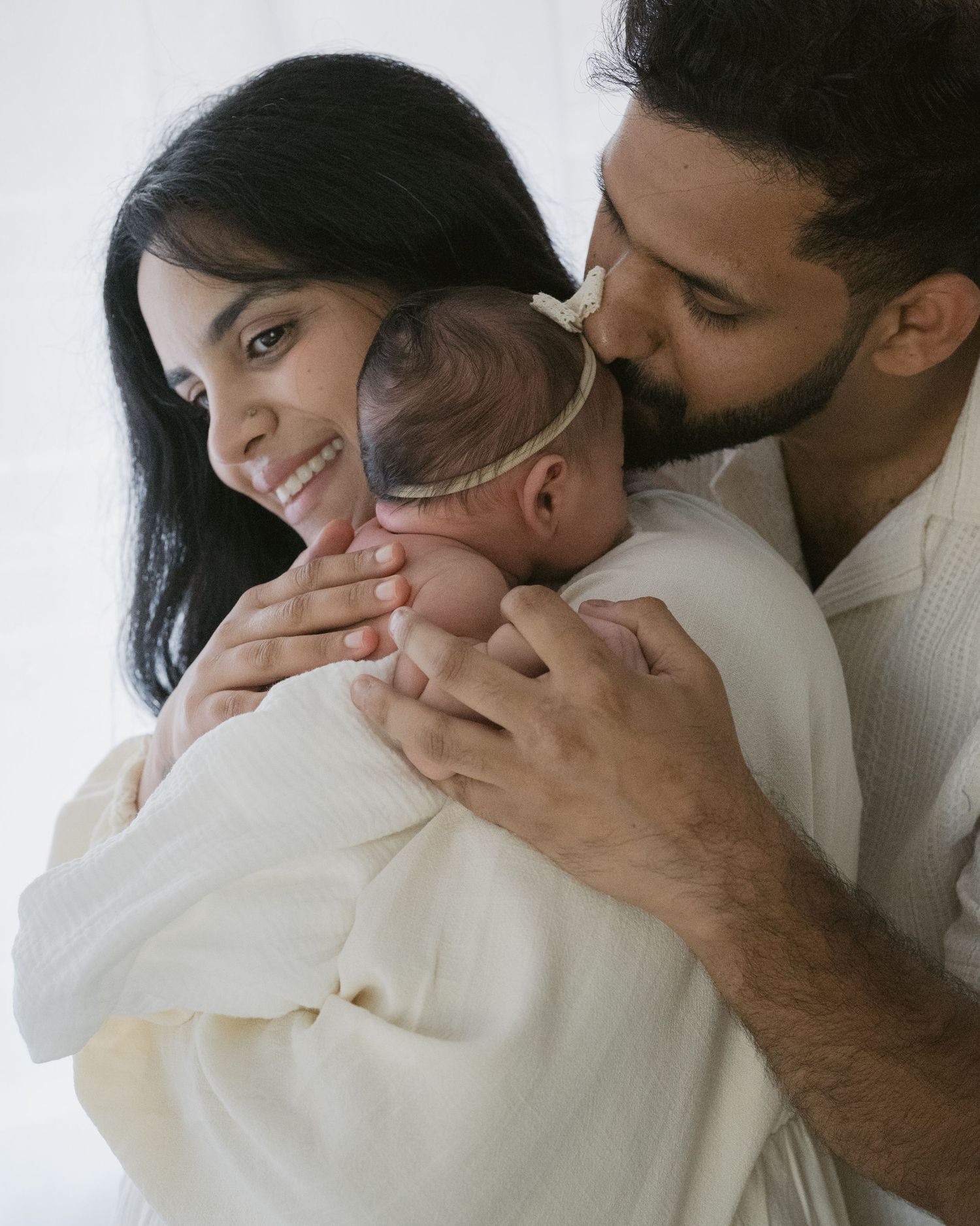 Mom holding her baby while Dad kisses baby’s forehead