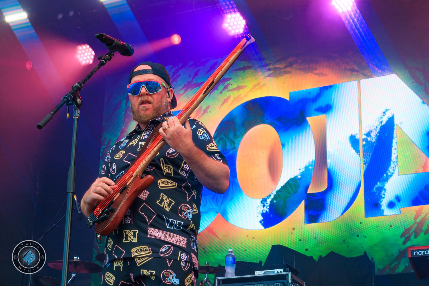 Musician playing electric violin on stage at outdoor music festival with colorful backdrop lighting.