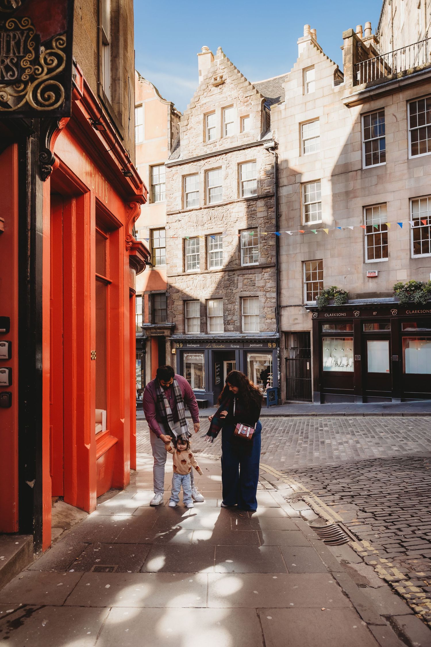 Family with young child exploring a charming cobblestone street in Edinburgh's Old Town on a sunny day.
