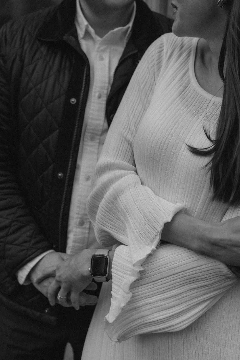 Close-up black and white engagement photo of a couple holding hands, showing intimate connection and natural emotion