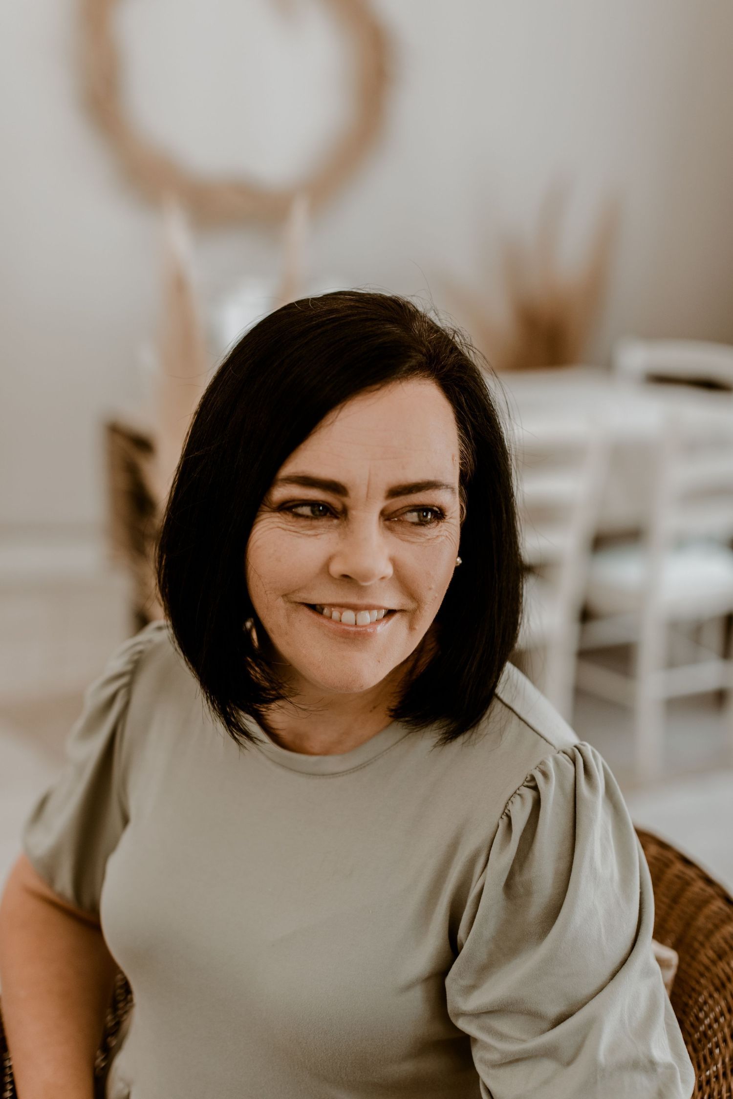 Woman smiling while using a Brother sewing machine, with a boho pampas grass wreath on the wall behind her.