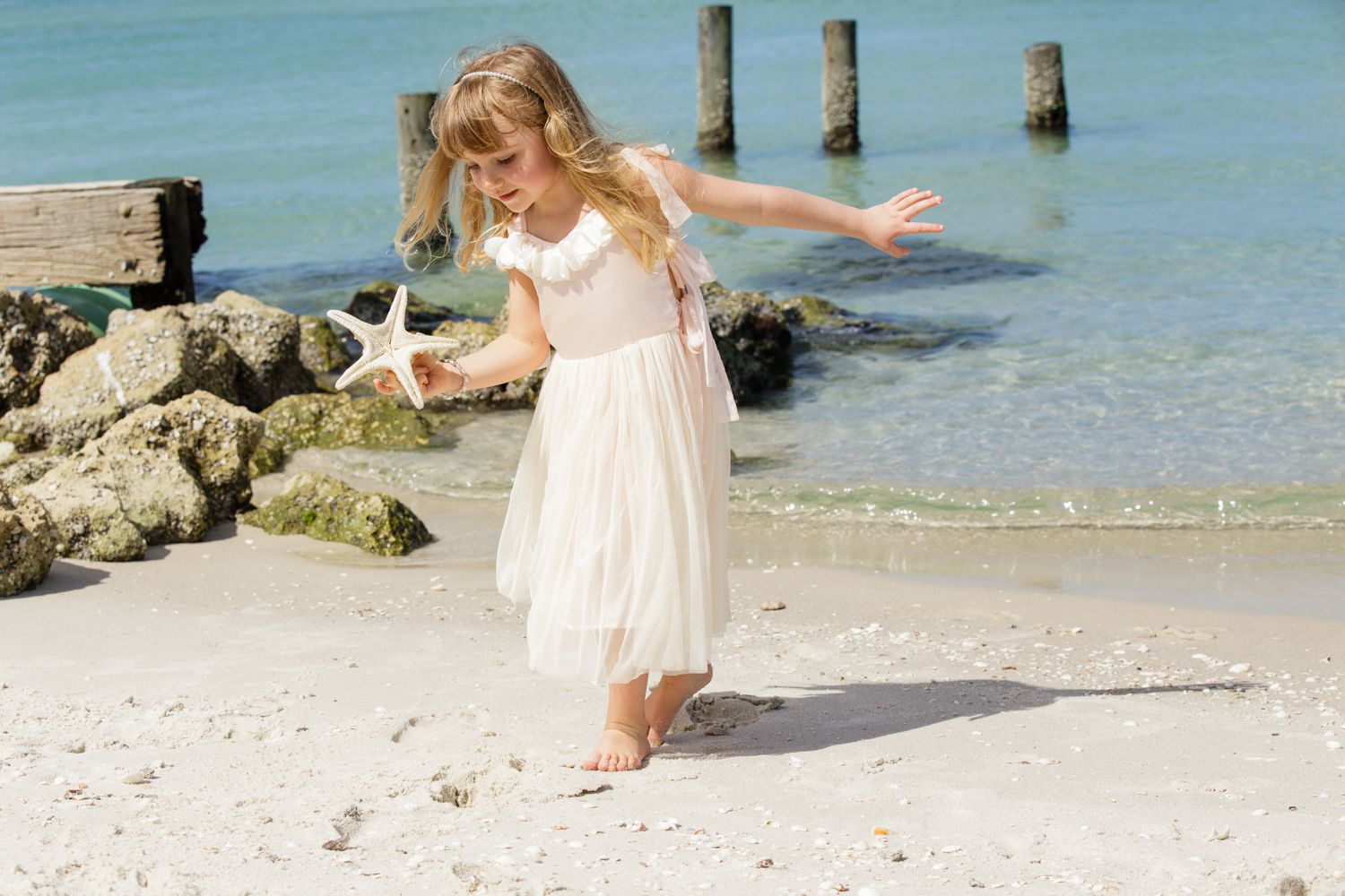 A girl holding a starfish walks on a sandy Naples FL beach with turquoise waters by Naples photographer, Mark Block