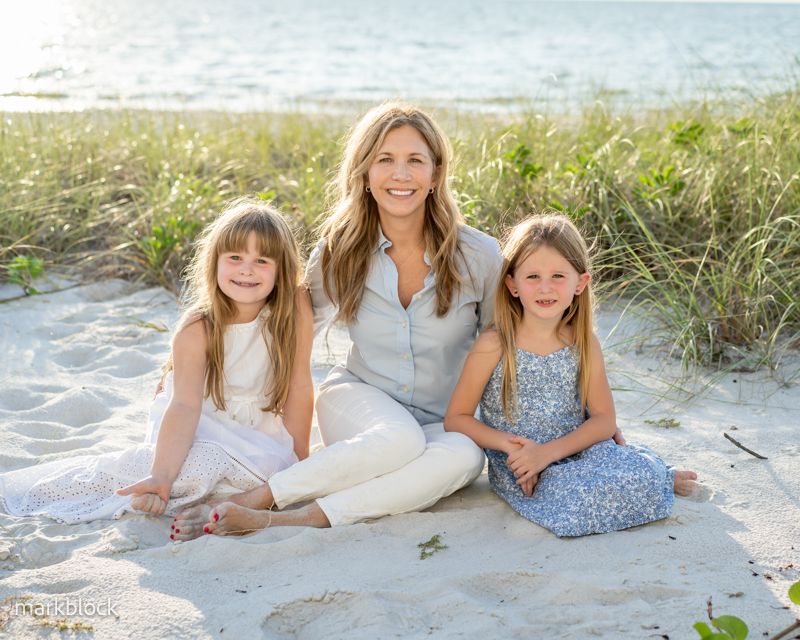 Naples FL family photo by Mark Block of three people in casual attire sitting together on Naples FL beach sand with sea grass backdrop.