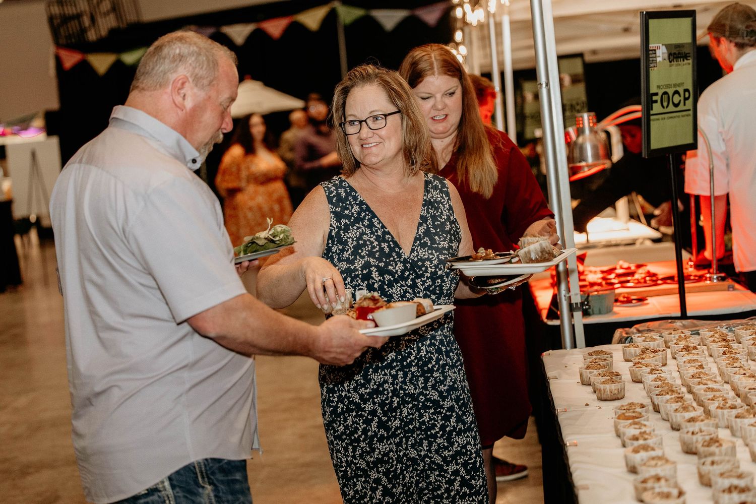 People gather at a festive event with drinks and appetizers in a warmly lit indoor venue.