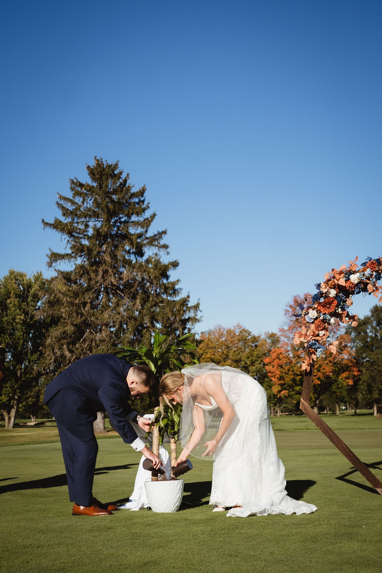 Sequence of wedding photos showing a couple playfully falling onto a grassy lawn at a golf course on a sunny autumn day.