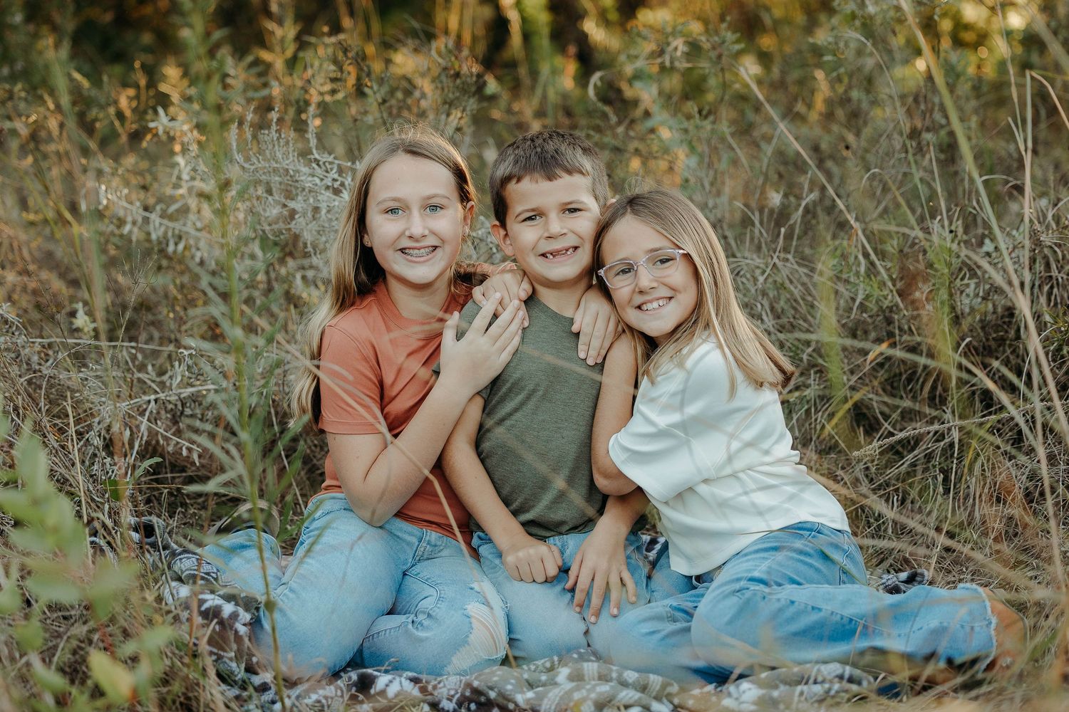 Children sitting together outdoors in casual clothing on natural terrain during golden hour lighting.