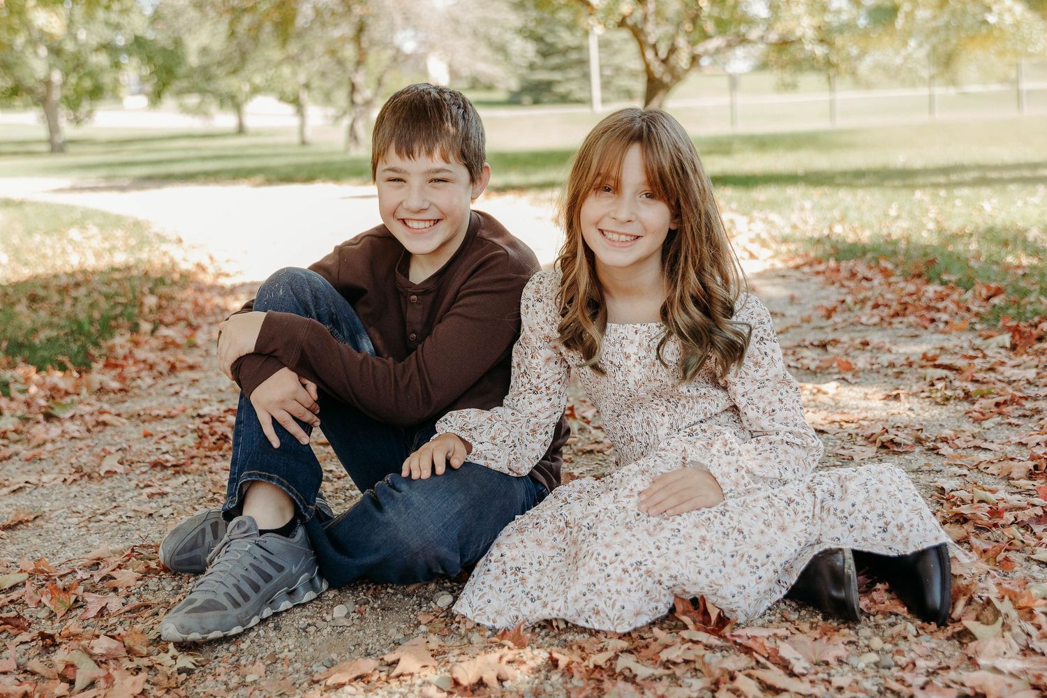 A couple lying in autumn leaves wearing cozy sweaters during an outdoor photoshoot.