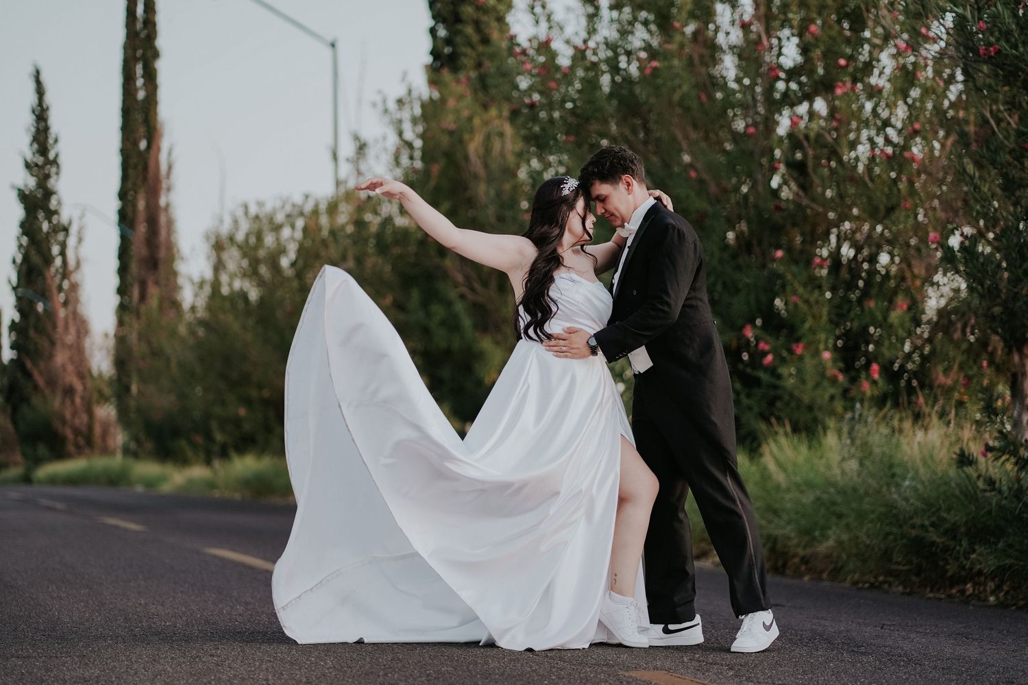 A wedding couple poses together in a series of romantic outdoor photos with flowing white dress and black suit.