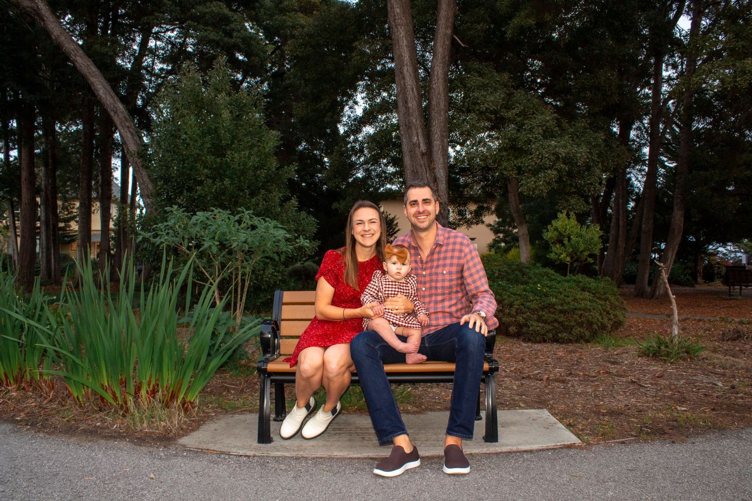 Happy couple sitting on a park bench holding a small child surrounded by lush greenery.