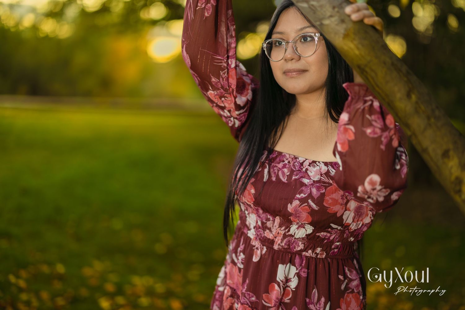 Person in floral burgundy dress posing under tree with golden sunset lighting.