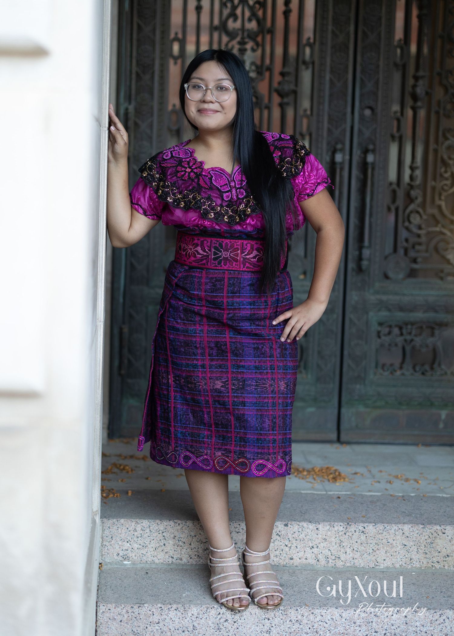 Portrait by ornate door showing person in purple patterned dress and sandals.