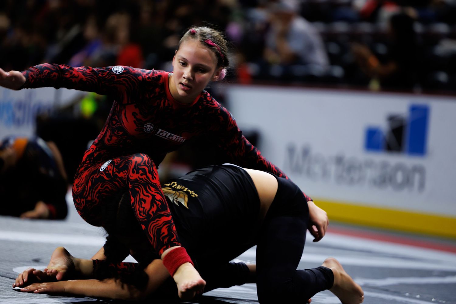 Competitors engaged in intense ground grappling during a martial arts tournament.