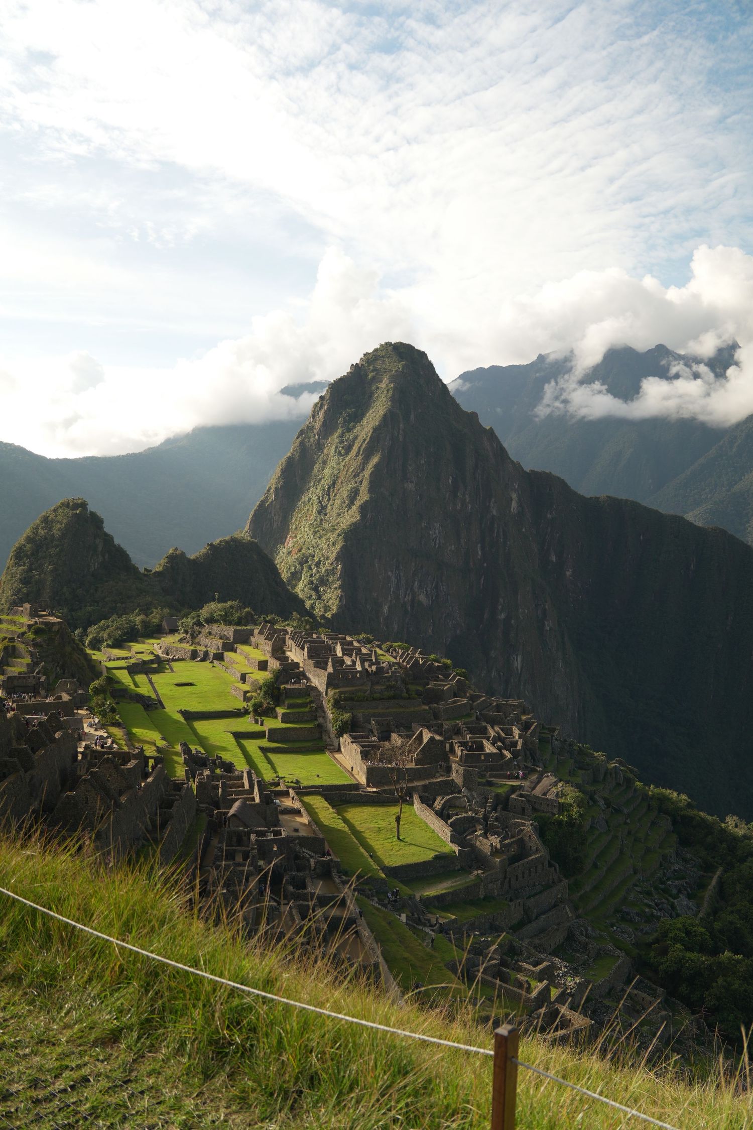 Aerial view of ancient Machu Picchu ruins with Huayna Picchu mountain peak emerging through clouds in Peru.