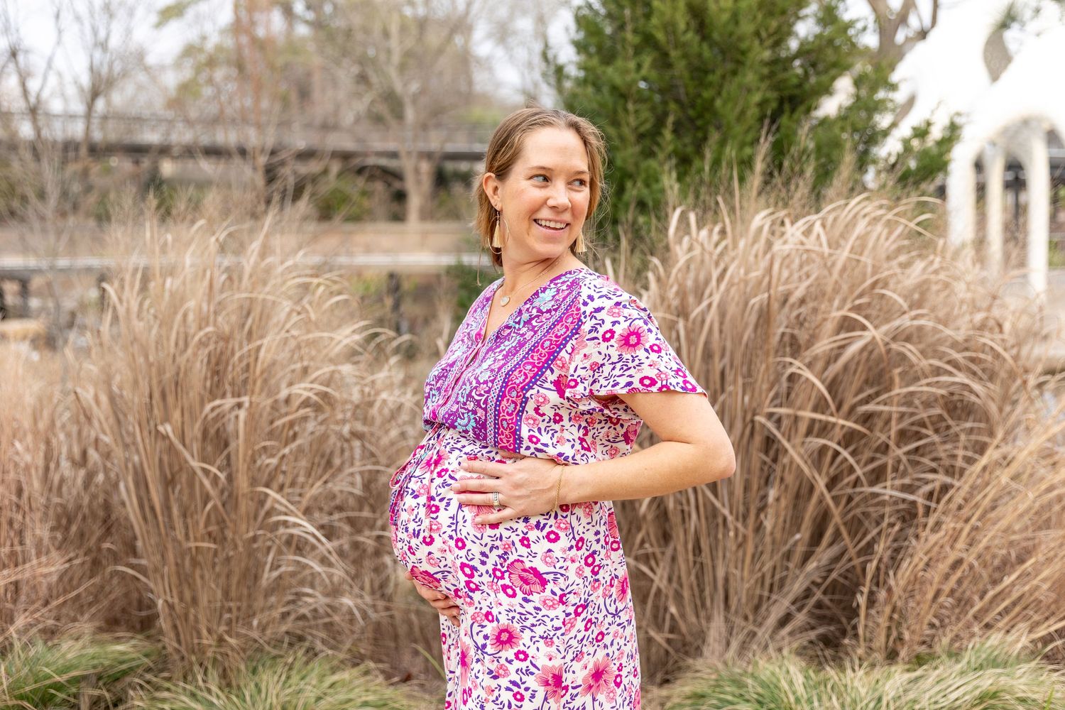 A person in a pink floral dress poses in front of tall ornamental grasses in a garden setting.