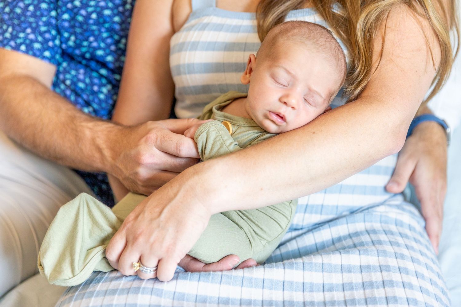 Sleeping newborn baby resting peacefully on mother's chest while father gently holds the infant.