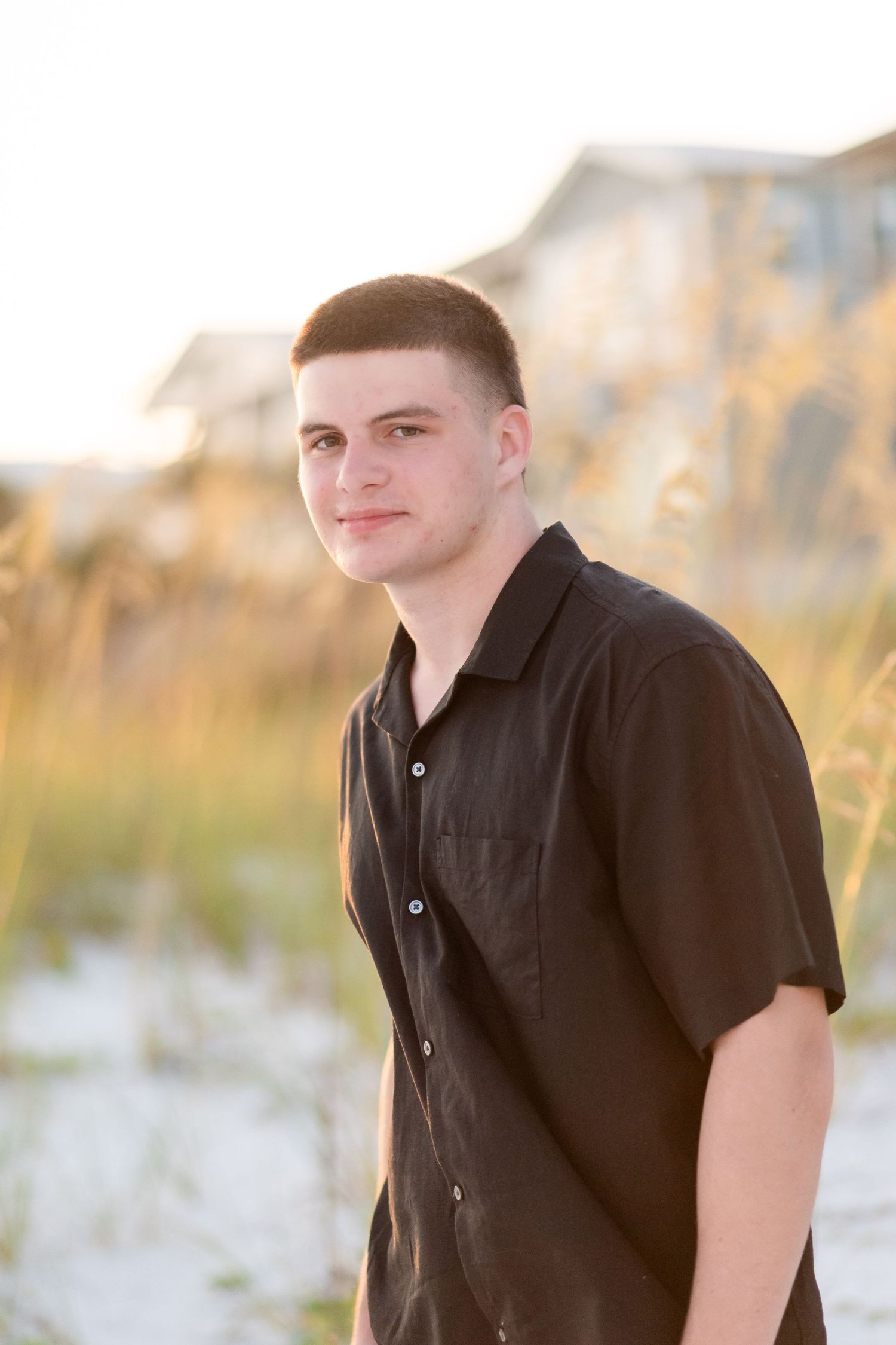 Person wearing a black polo shirt poses outdoors at sunset with golden grass in the background.