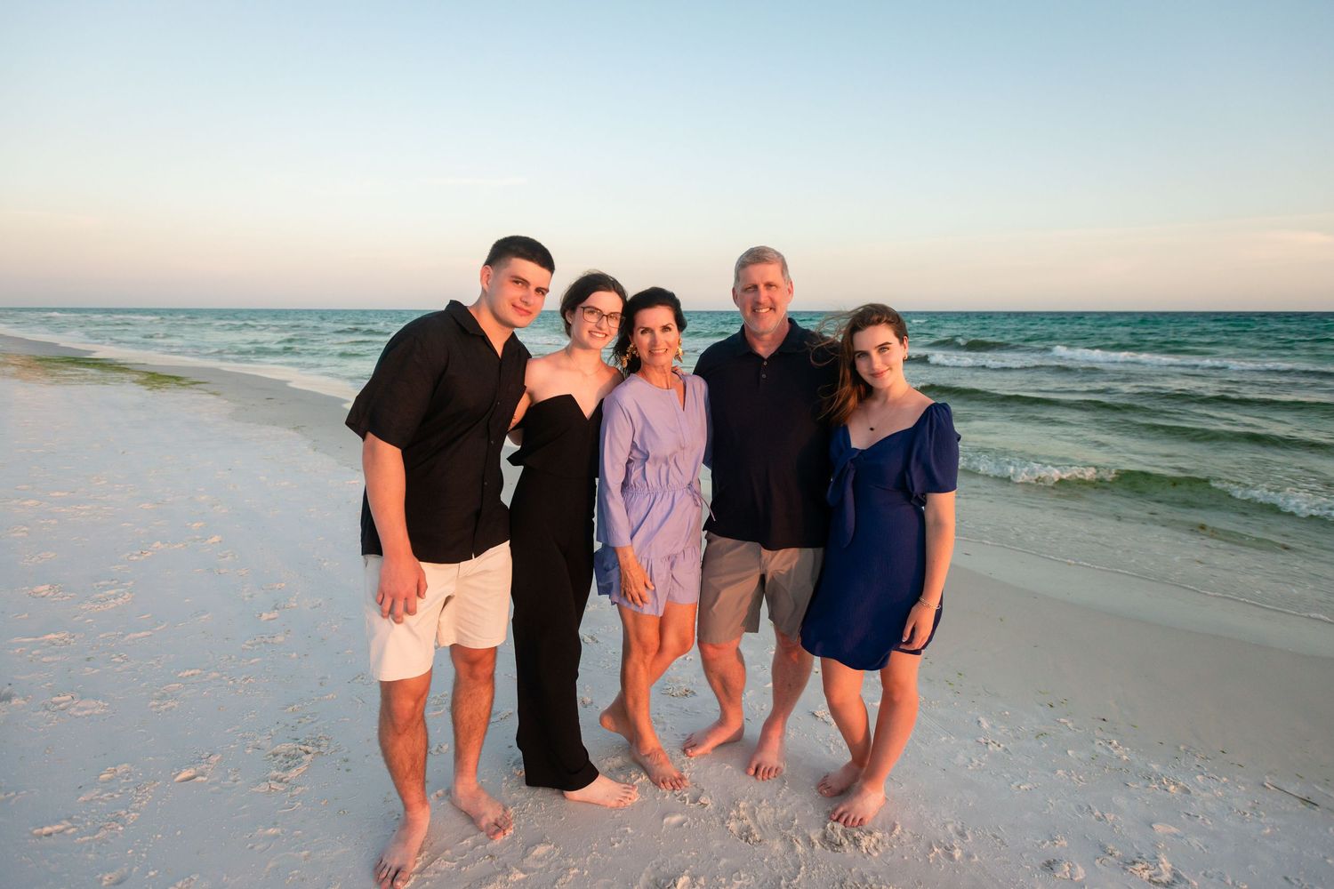 Group of people walking along a scenic beach at sunset with waves crashing on the shore in the background.