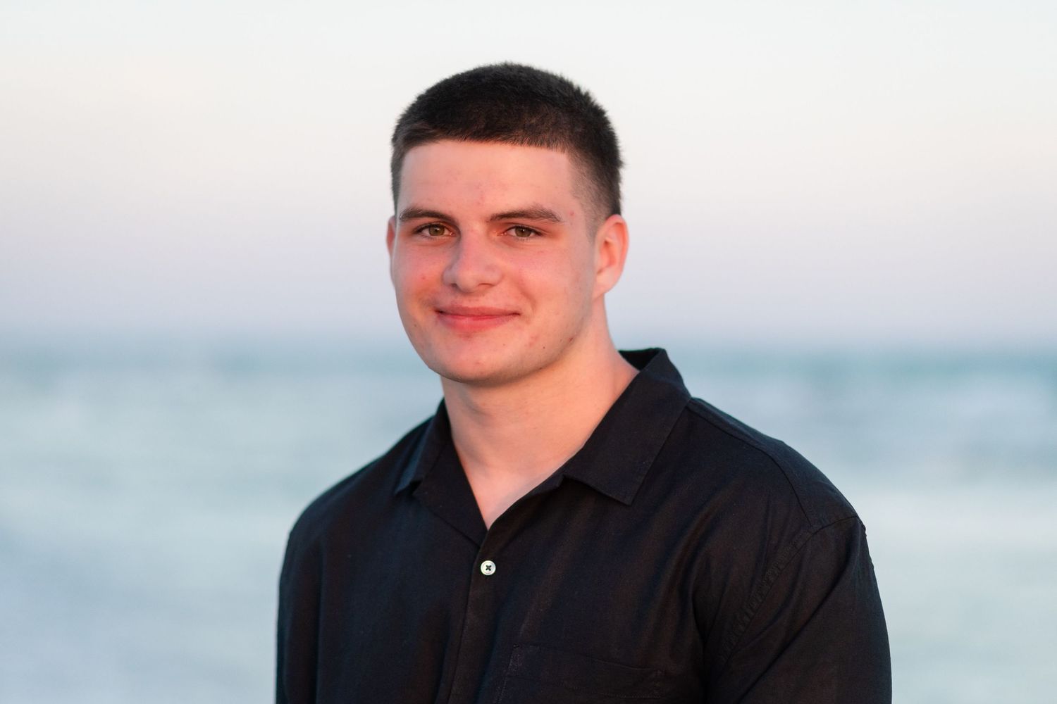 Person in a black shirt smiles while posing against a bright white background.