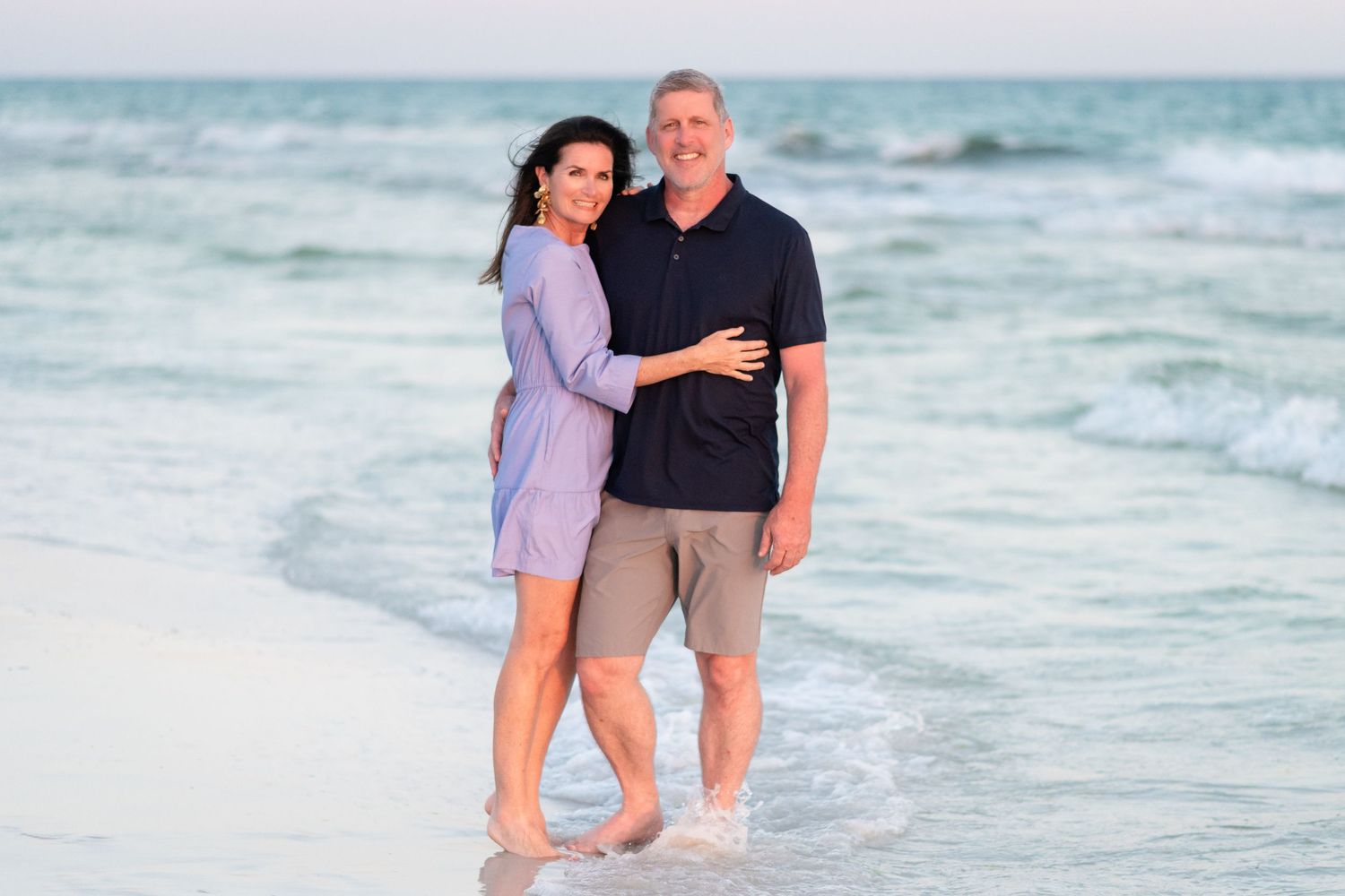 Couple walking together and splashing in the waves along a scenic beach at sunset.
