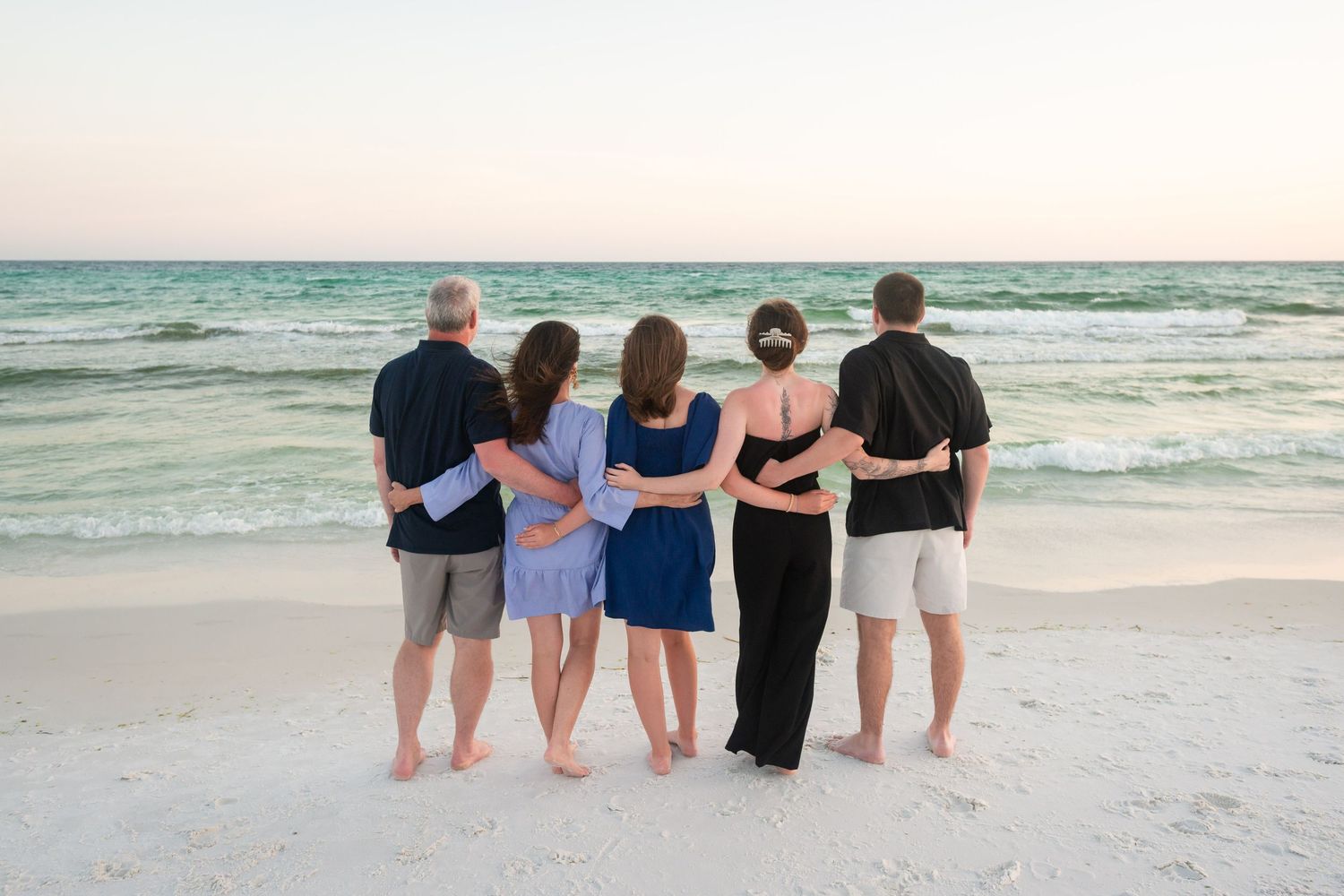 A group of people sitting together on a sandy beach watching the ocean waves at sunset.