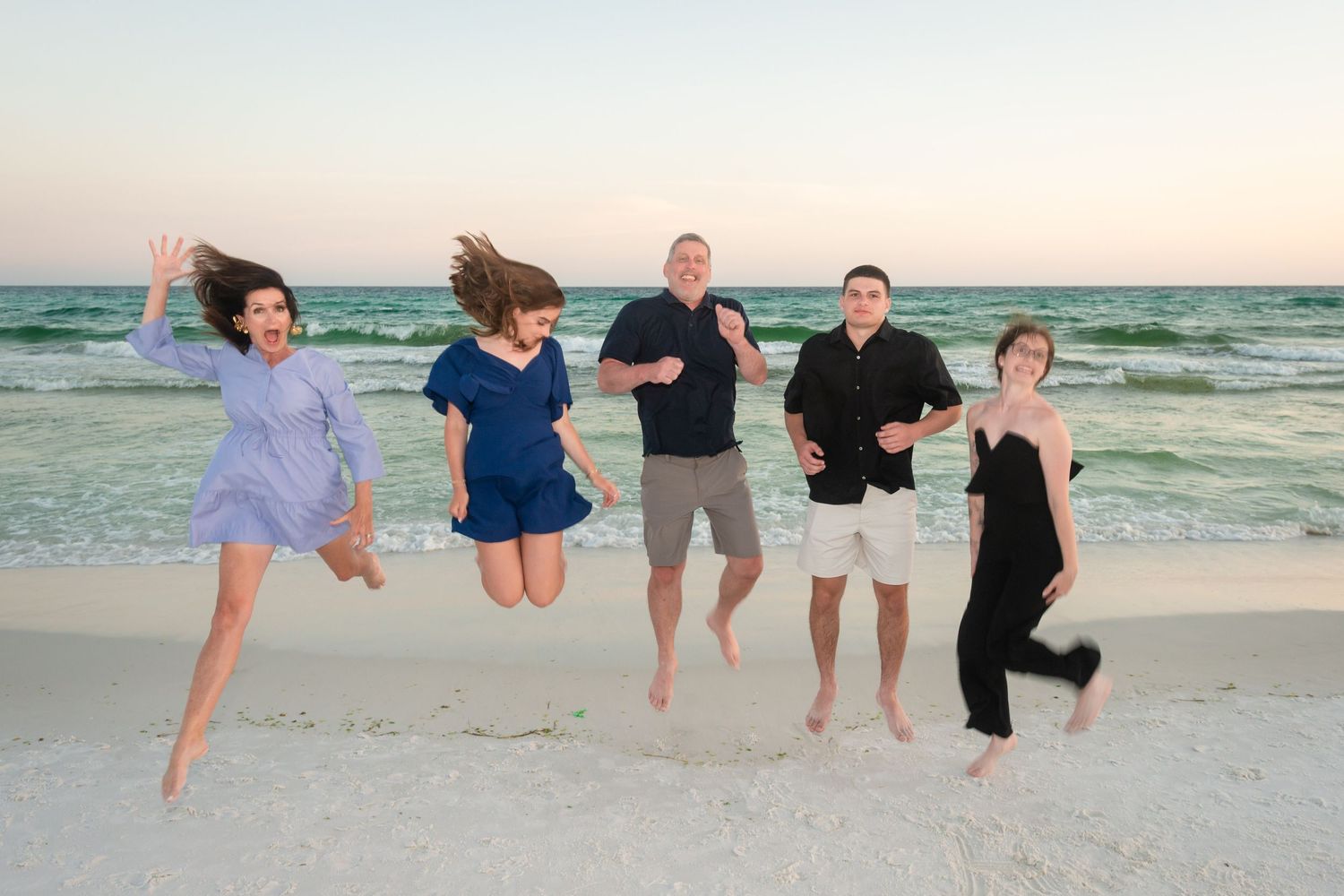 Group of people walking along the beach at sunset with their feet in the sand and ocean waves in the background.