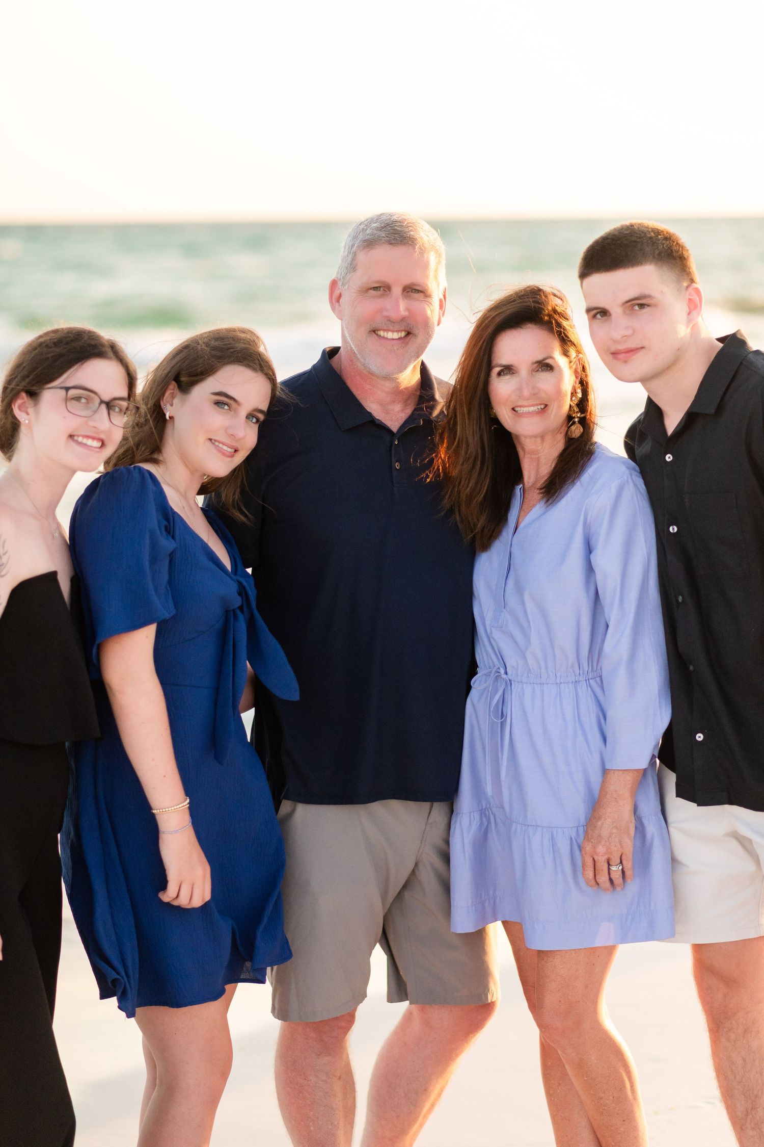 A group in coordinated navy and light blue outfits poses together on a beach during a casual photo session.
