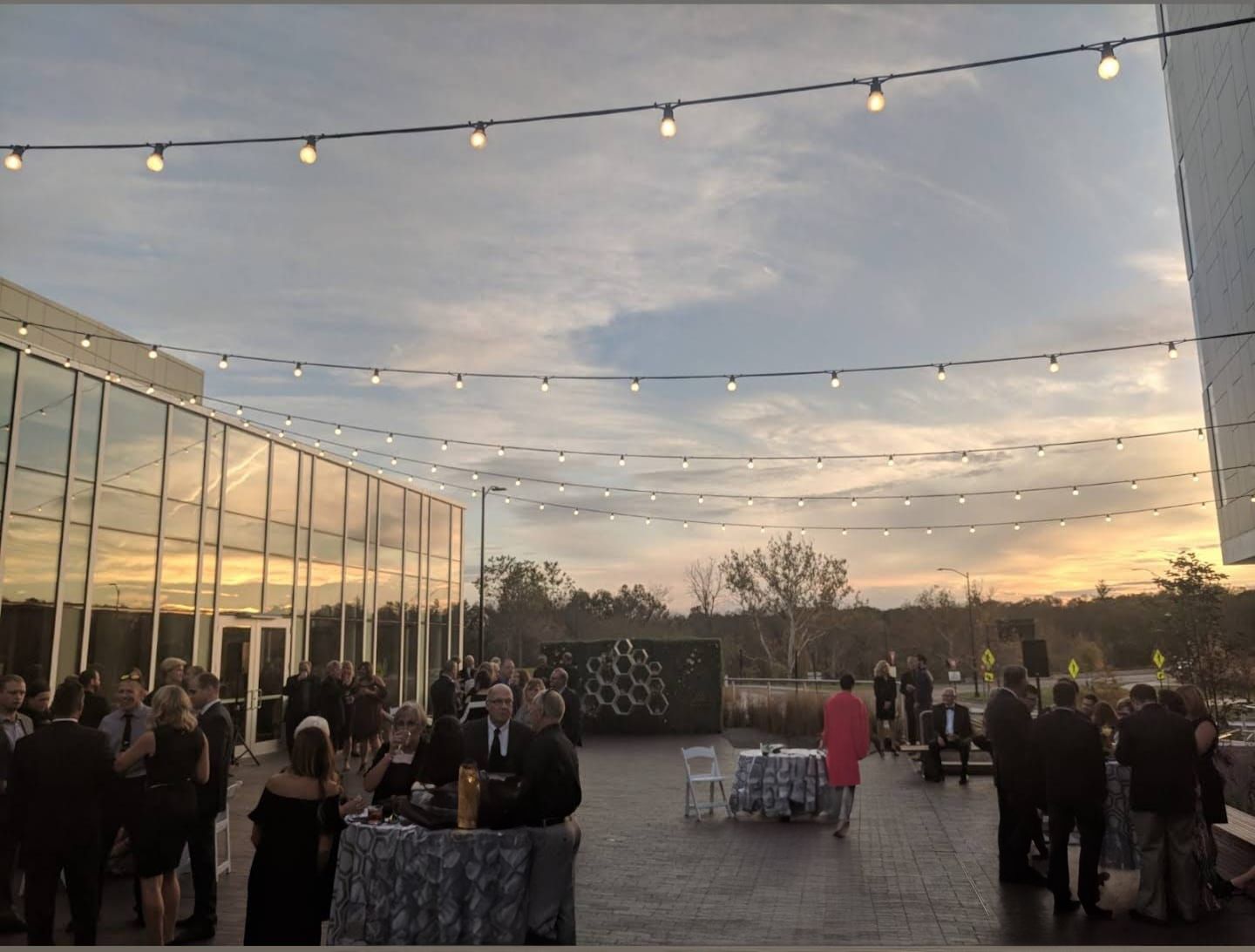String lights illuminate an outdoor wedding reception space at dusk with dramatic sky views.