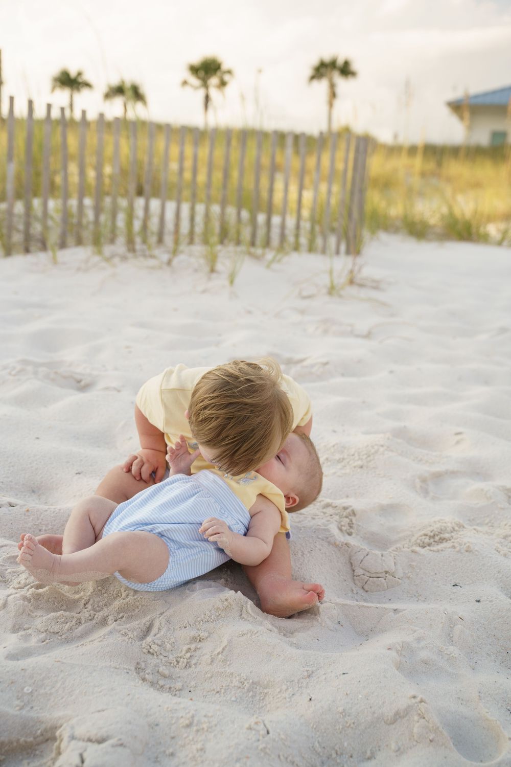 Two small children share a sweet moment while playing in the white sand at the beach.