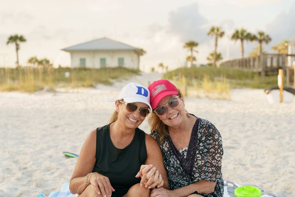 People enjoying a romantic sunset beach picnic with wine glasses and snacks while sitting on a blanket in the sand.