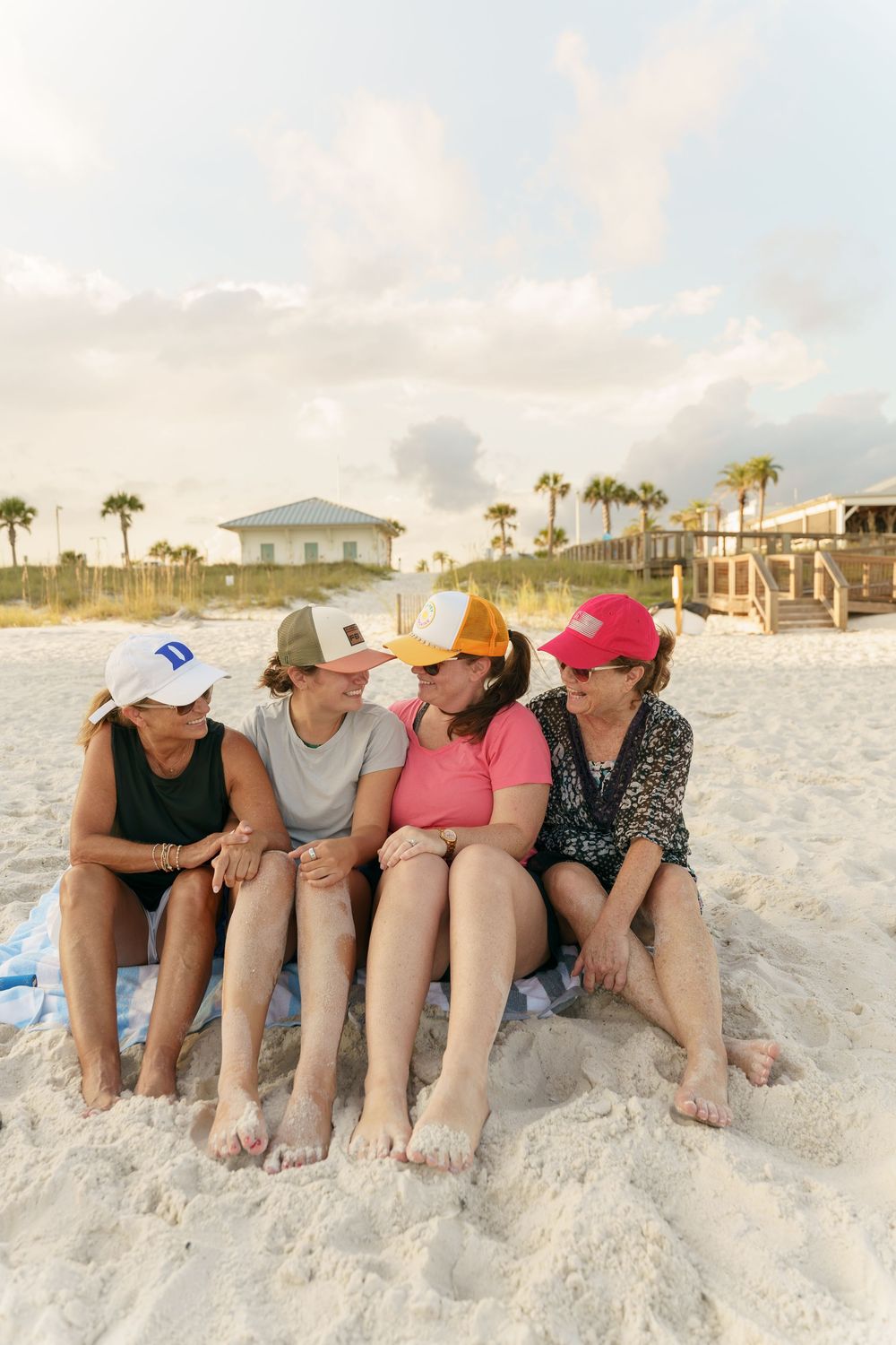 Four friends in casual beachwear sit together on the sand enjoying a beach day.