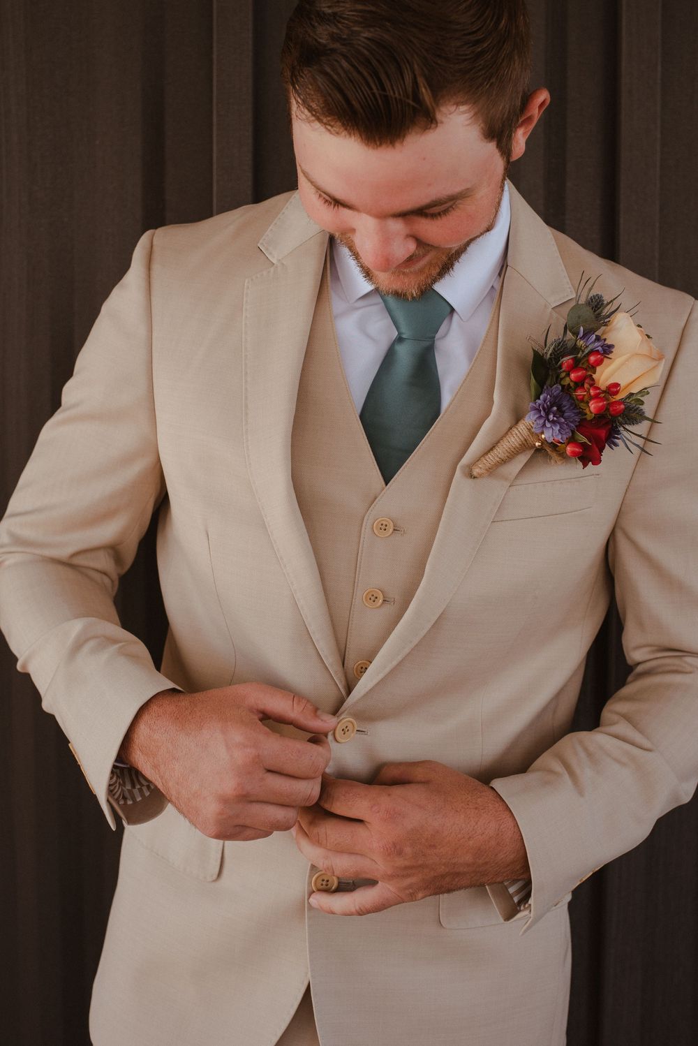 Close-up shots of a groom in a beige suit adjusting his boutonniere featuring red and blue flowers.
