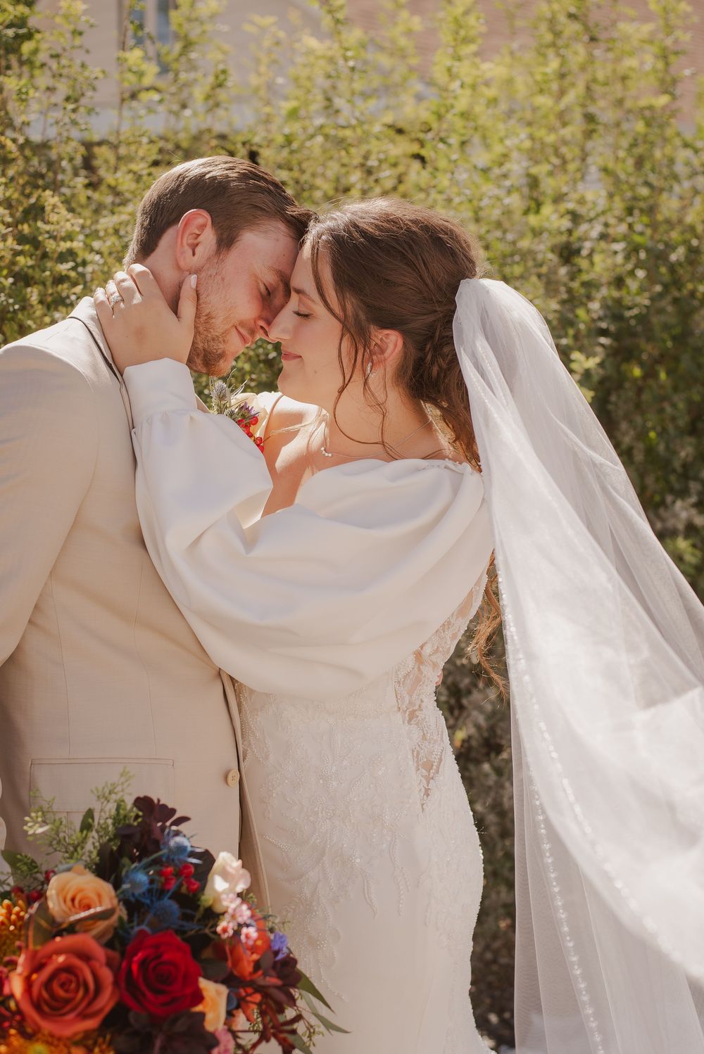 Newlyweds share intimate moments against a natural backdrop with colorful floral accents.