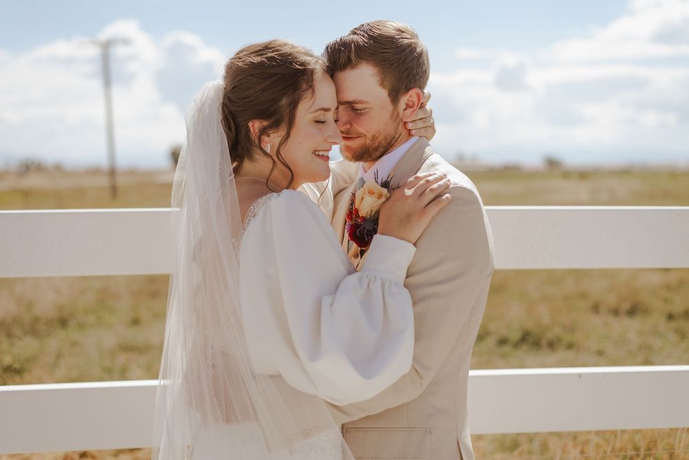 Intimate wedding portraits in an open field with white fence and cloudy sky backdrop.