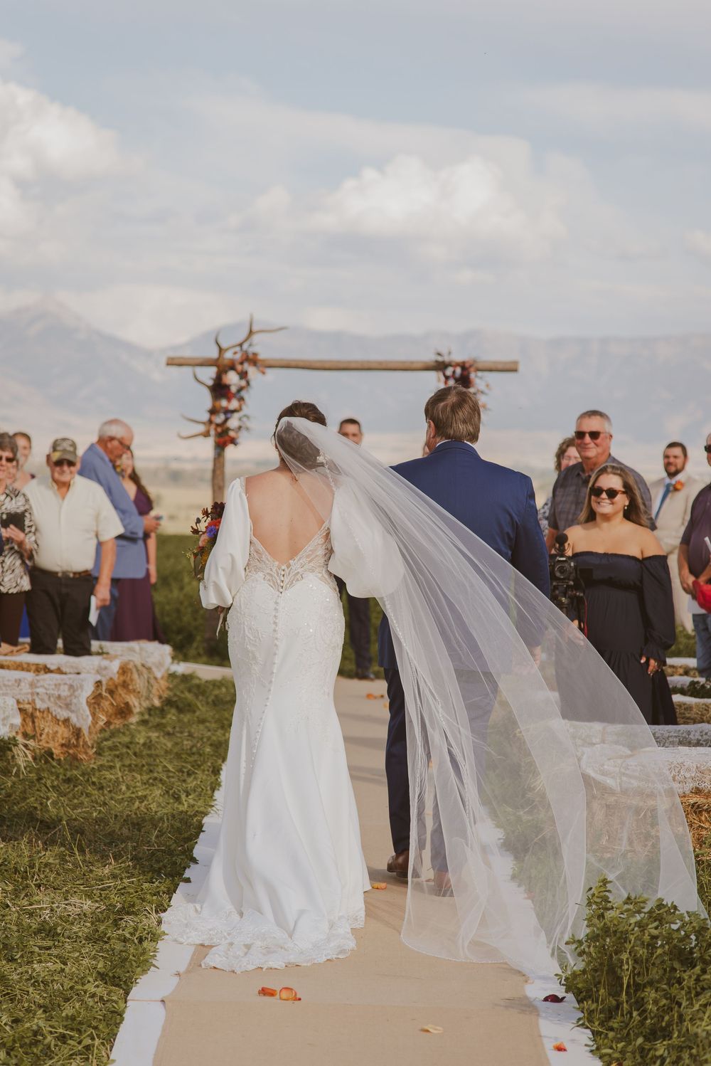 Outdoor wedding ceremony with rustic wooden arch and guests gathered in natural setting.