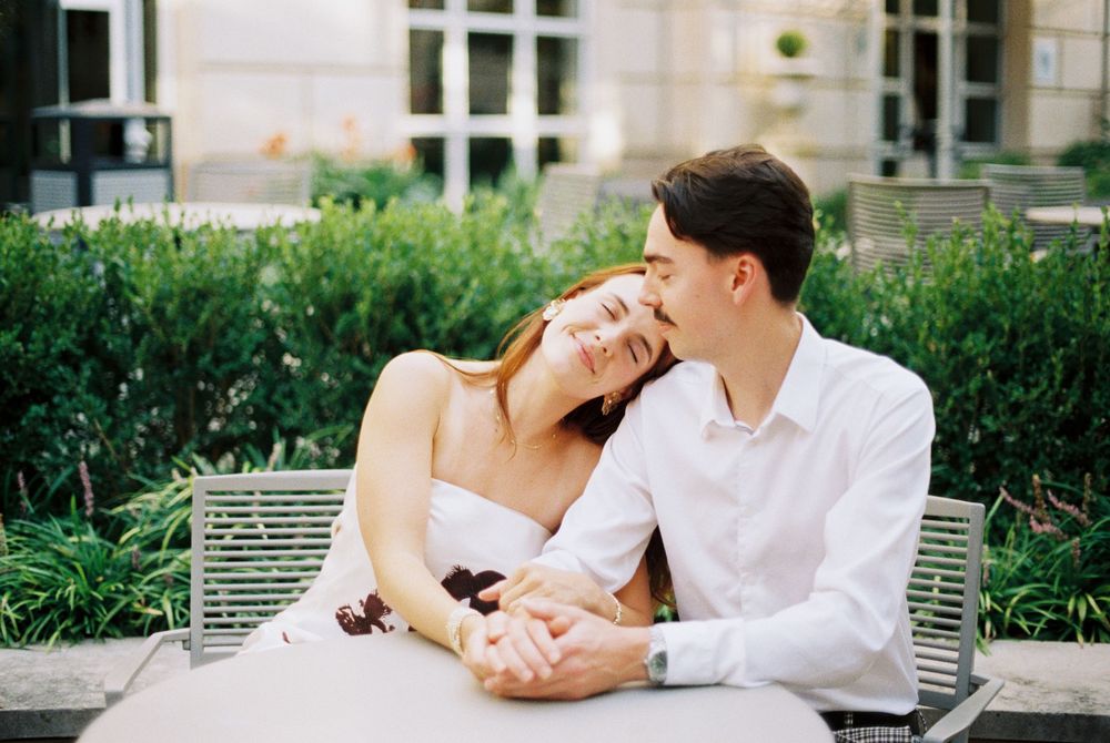 A couple sits together on a white bench in a garden setting while sharing an intimate moment.