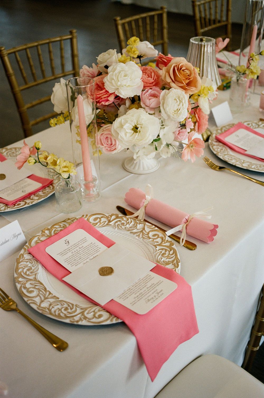Elegant wedding table setting with pink napkins, gold charger plates, floral centerpiece, and pink taper candles.